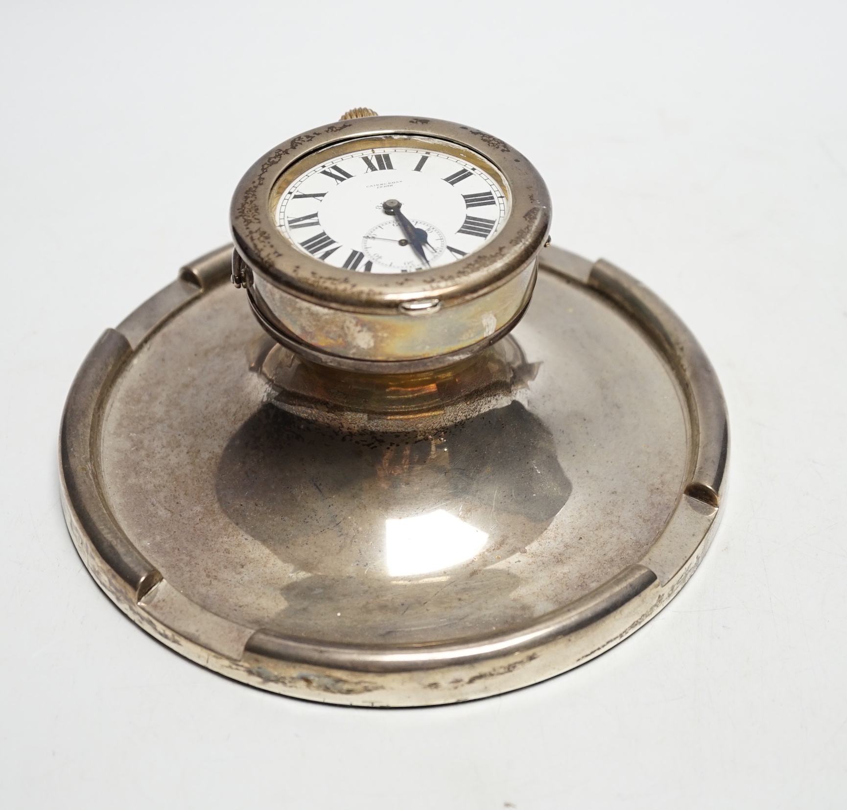 A George V silver mounted combination inkwell/pocket watch holder, Birmingham, 1926, containing an eight day pocket watch, Cairncross, Perth, base diameter 17.7cm.